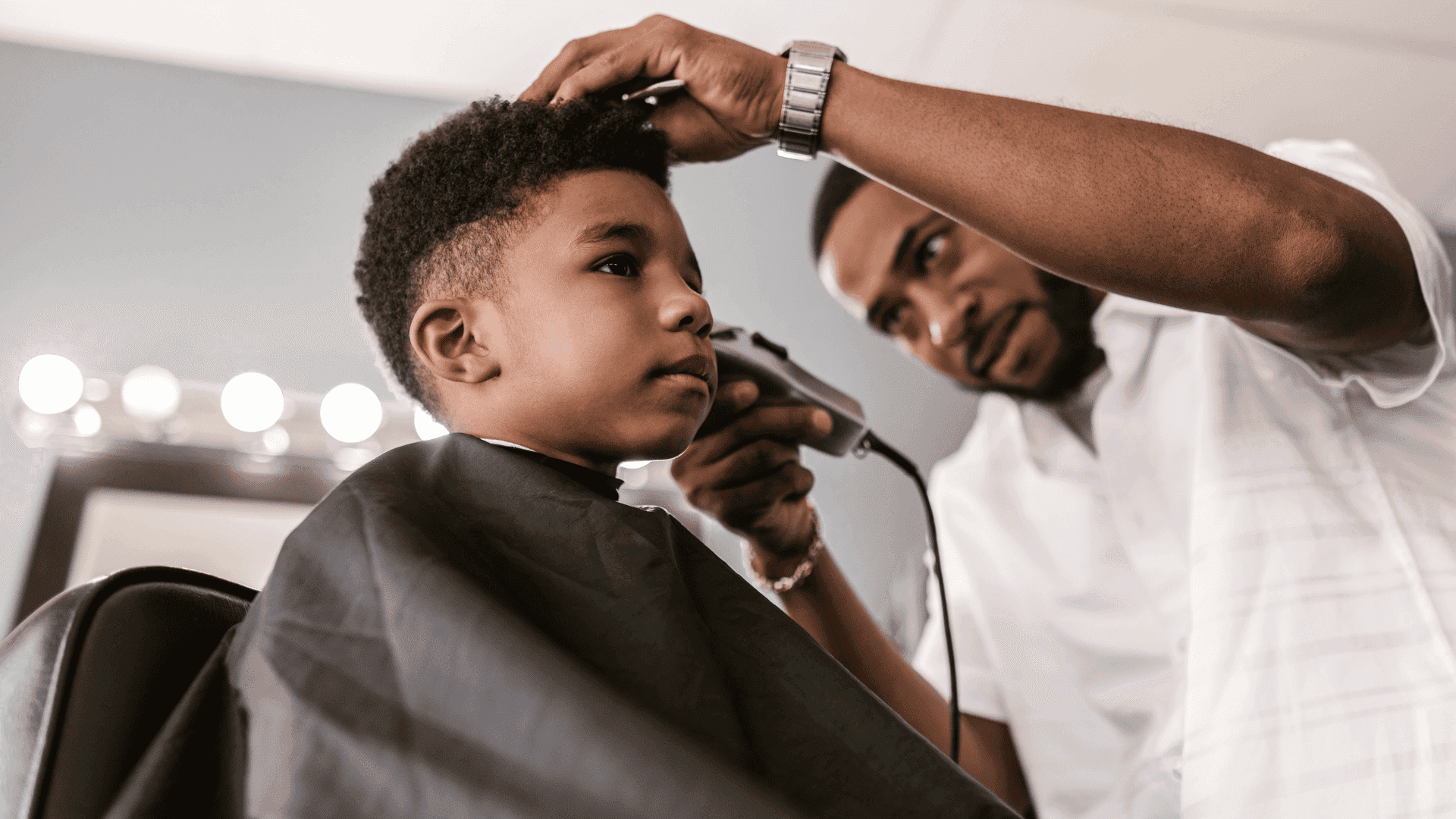 Child getting a haircut from barber using clippers in a salon.