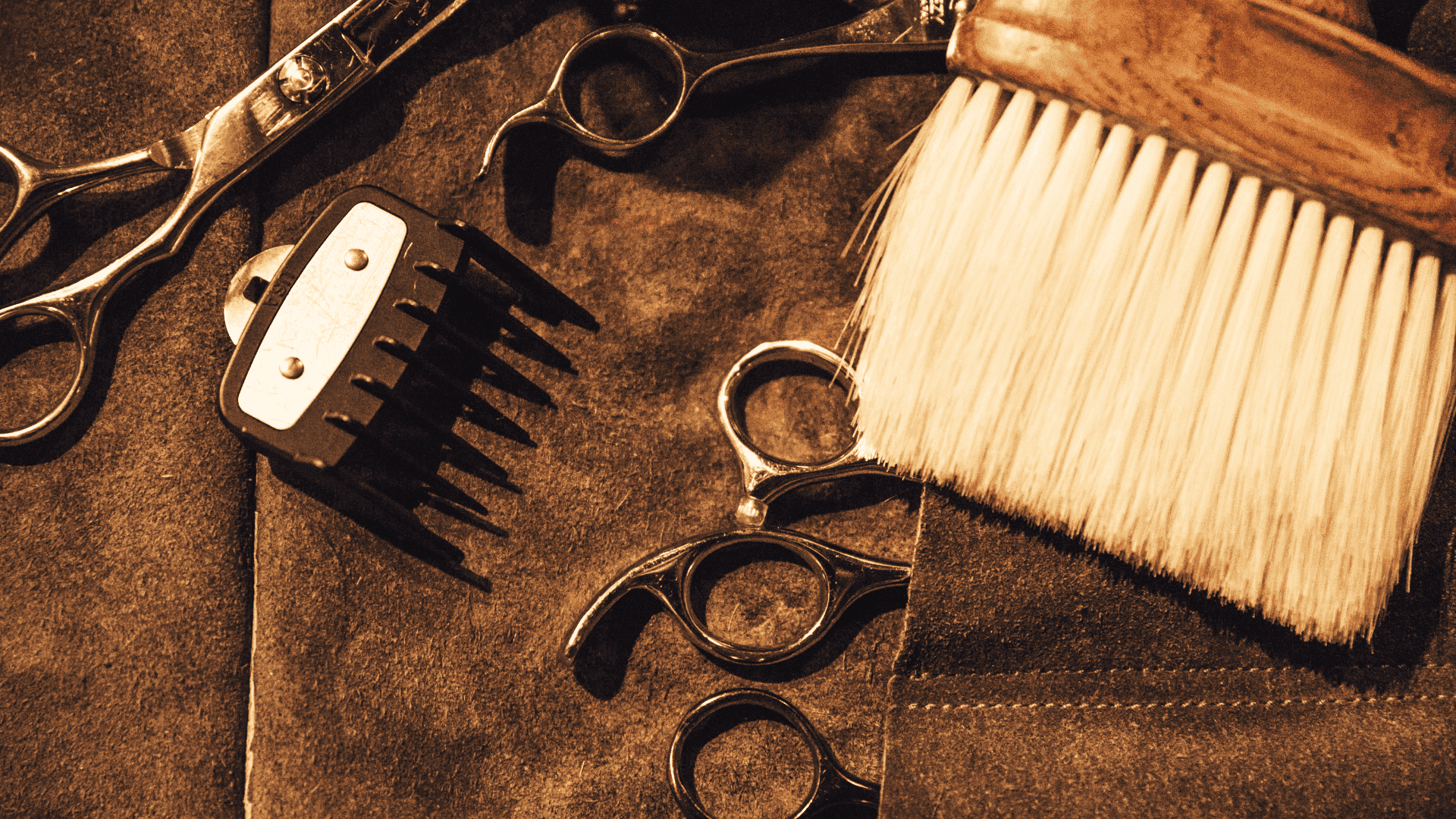 Barber tools on a leather apron: scissors, brush, and clipper attachment.