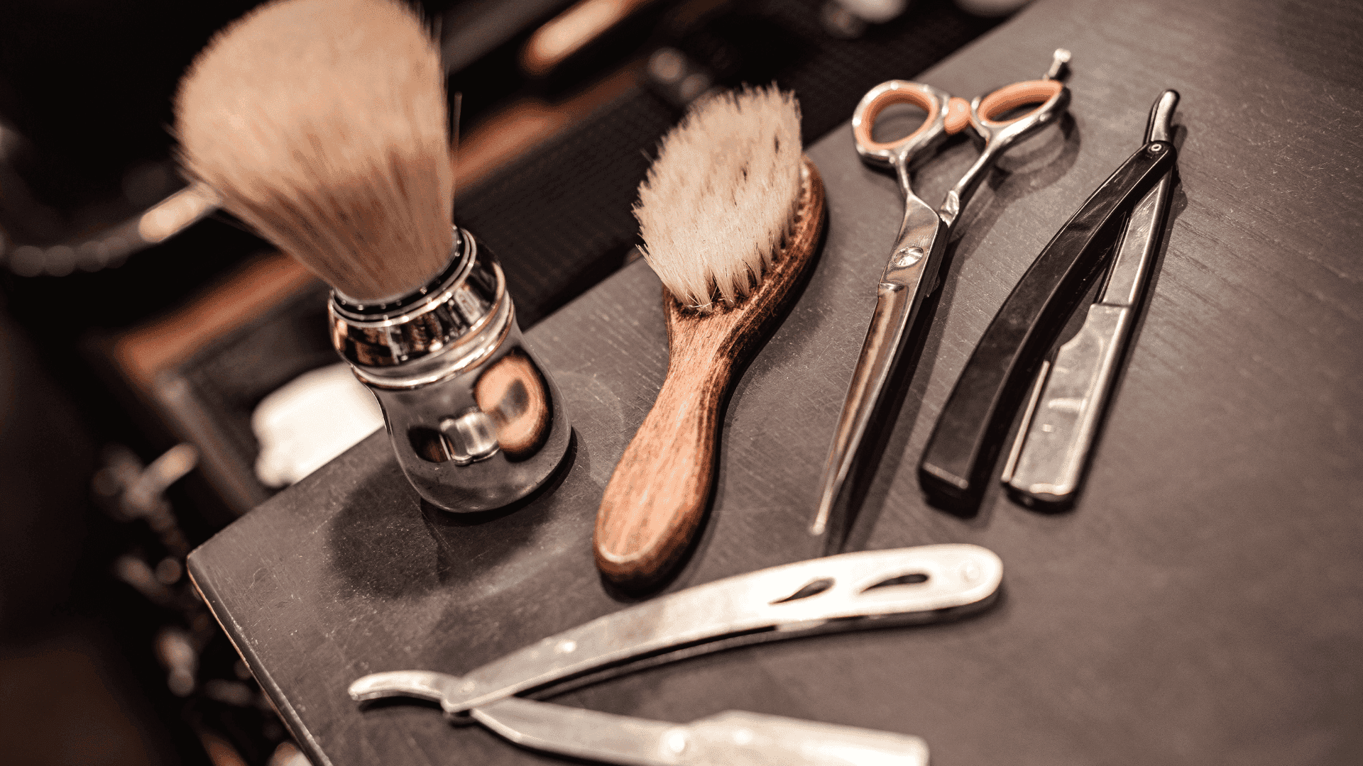 Barber tools with brushes, scissors, and razors on a dark wooden surface.